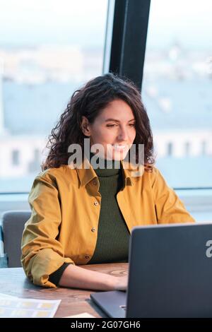 Junge lächelnde Frau, die am Tisch sitzt und im Büro am Computer arbeitet Stockfoto