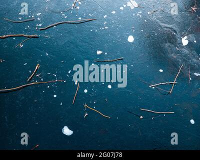 Die Eisoberfläche eines gefrorenen Sees ist mit trockenen Ästen bedeckt. Winterhintergrund. Stockfoto