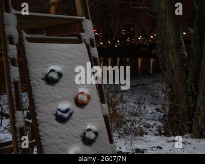 Eine schneebedeckte Kletterwand auf dem Kinderspielplatz. Nächtliches Stadtbild mit Lichtern, die sich im Fluss spiegeln. Winterhintergrund. Stockfoto