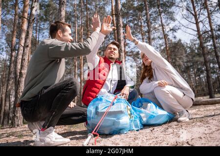 Fröhliche Freiwillige, die in der Nähe von Müllsäcken im Wald hohe fünf geben Stockfoto