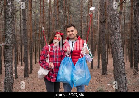 Glückliches Paar mit Müllsäcken, die im Wald Pick-up-Werkzeuge halten Stockfoto