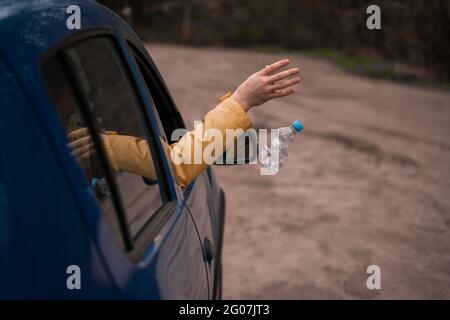 Beschnittene Ansicht eines Mannes, der leere Plastikflaschen aus dem Auto wegwirft Stockfoto