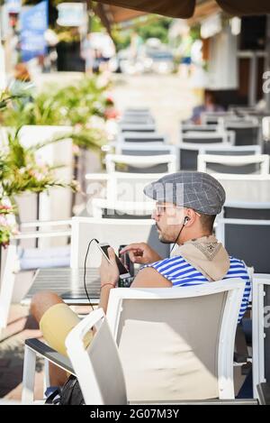 Sotschi, Russland, 27. Juli 2019: Reisender Mann sitzt mit dem Rücken in einem Café auf dem Pier, hört Musik auf einem Smartphone und schaut weg Sotschi. Sommer tim Stockfoto