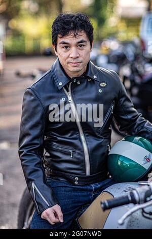 Asiatischer Mann in schwarzer Lederjacke sitzt auf dem Motorrad und hält einen Helm. Stockfoto