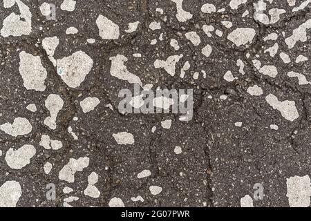 Getrocknete weiße Farbflecken auf beschädigtem, rissigem Asphalt der alten Straße. Abstrakt gemusterter Hintergrund Stockfoto