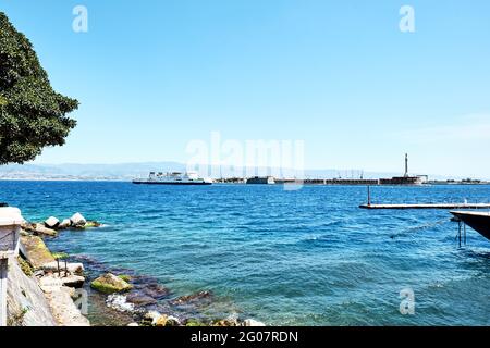 Messina, Sizilien, Italien - 26. April 2021: Hafen von Messina mit festfahrenden Booten, goldener Madonna della Lettera Statue und kalabrien Küste im Hintergrund. Stockfoto