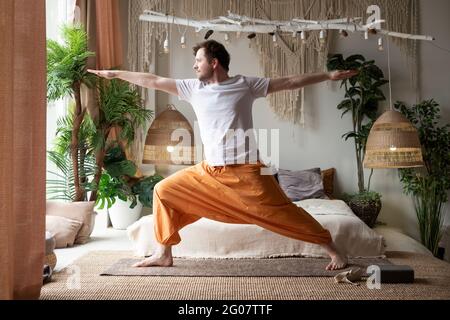 Mann, der Yoga praktiziert und Kriegerpose oder virabhadrasana zu Hause macht Stockfoto