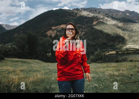 Frau, die im Wald mit Bergen den Dandelion bläst Stockfoto