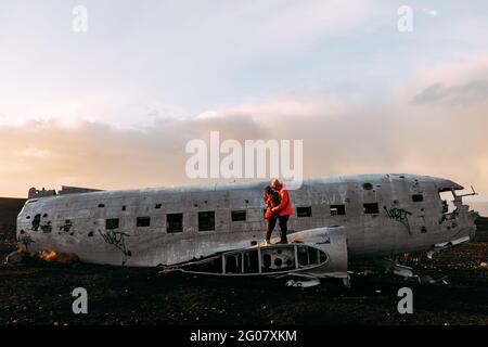 Junges Paar, das auf zerstörten Flugzeugen zwischen einsamen Ländern und steht Blauer Himmel Stockfoto