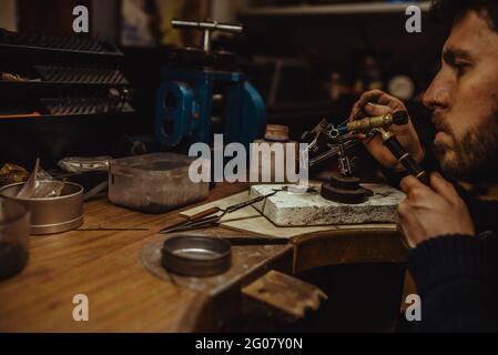 Goldschmied verwendet eine Lötlampe, um beim Herstellen kleine Metallornamente zu erhitzen Schmuck auf der Werkbank Stockfoto