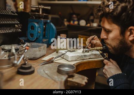 Goldschmied verwendet eine Lötlampe, um beim Herstellen kleine Metallornamente zu erhitzen Schmuck auf der Werkbank Stockfoto