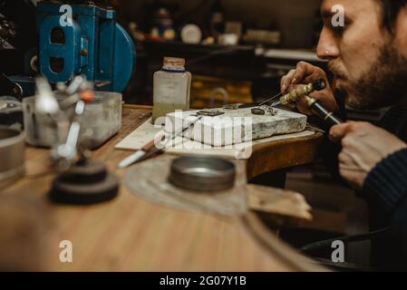 Goldschmied verwendet eine Lötlampe, um beim Herstellen kleine Metallornamente zu erhitzen Schmuck auf der Werkbank Stockfoto