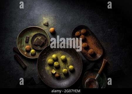 Overhead große Platte mit grünen Trüffel Matcha und Platte mit Braune Trüffelkugeln mit Pulver und Sieb und Schokoladenstücken Stockfoto