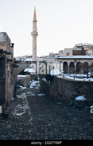 Leere Straße mit Pflastersteinen führt zwischen alten Gebäuden zu Hoher Minarett-Turm gegen klaren blauen Himmel in der Türkei Winterzeit Stockfoto