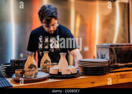 Junger Mann auf der Schürze kocht asiatische Gerichte, während er steht Theke in Ramen Bar Stockfoto