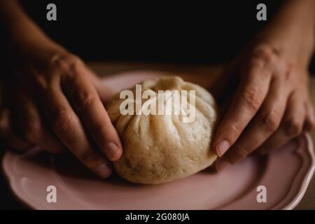 Hände einer Frau mittleren Alters, die ein gedämpftes Baozi-Brötchen auf eine Keramikplatte legt Stockfoto