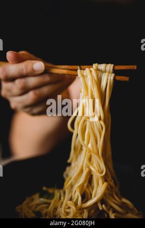 Hand einer Frau, die Bambusstäbchen mit leckeren Weizennudeln vom chinesischen Ramen-Teller hält Stockfoto