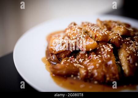 Leckeres würziges Huhn auf weißem Teller auf Holztisch zubereitet Im asiatischen Restaurant Stockfoto