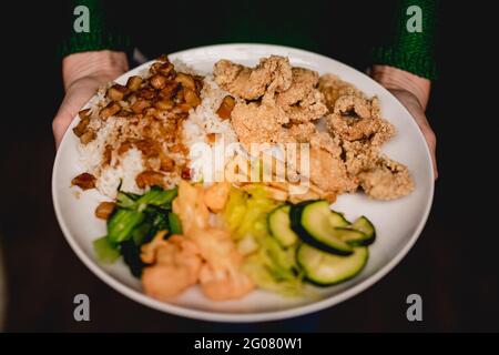 Von oben die Hände der Frau, die schmackhaftes taiwanesisches Bento auf dem Holztisch im asiatischen Café hält Stockfoto