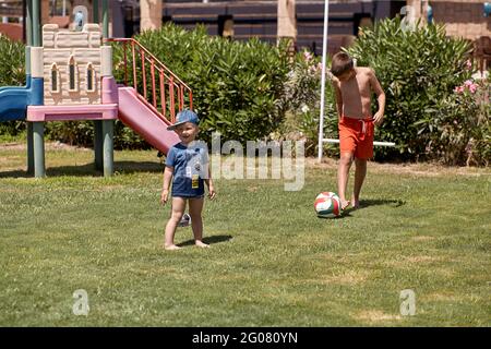 Kemer, Türkei - Mai, 21: Kleinkind und Teenager spielen bei sonnigem Wetter auf grünem, frischem Rasen Fußball. Konzept von sozialer Distanz, Sommerspaß und Urlaub. Hochwertige Fotos Stockfoto