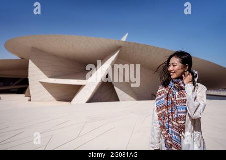 Glückliche asiatische Frau lächelt weg, während sie vor der prächtigen Fassade des Nationalmuseums mit ungewöhnlicher Architektur steht, die aus vielen CI besteht Stockfoto