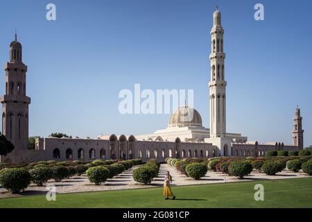 Nicht erkennbares Weibchen in Kleidern, das auf grünem Rasen in der Nähe von Sultan steht Qaboos große Moschee befindet sich in der Provinz Maskat von Oman in Sonniger Tag mit blauem Himmel Stockfoto