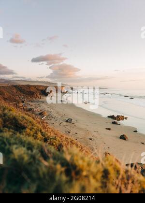 Hoher Winkel der wunderbaren Landschaft des stürmischen Ozeans Wasser mit Schaumwellen waschen den Sandstrand gegen die neblige Hochlandküste unter Grauer Himmel in Big Sur Stockfoto