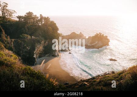 Hoher Winkel der wunderbaren Landschaft des stürmischen Ozeans Wasser mit Schaumwellen waschen den Sandstrand gegen die neblige Hochlandküste unter Grauer Himmel in Big Sur Stockfoto