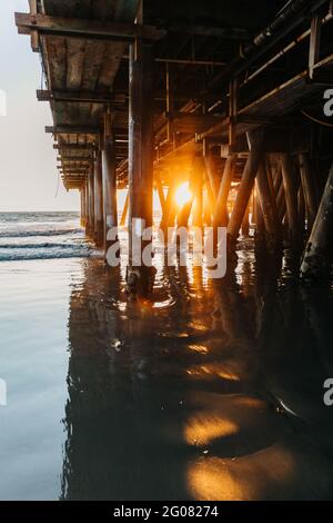 Glühendes Sonnenlicht durchdringt abends die Berge von Santa Monica pier mit friedlichen Wellen am Strand in Kalifornien Stockfoto