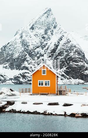 Gelbe Hütte in der Nähe der schneebedeckten Küste der Bergkette auf den Lofoten-Inseln, Norwegen Stockfoto