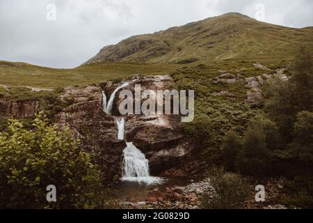 Malerischer Blick auf den kleinen Wasserfall in Felsen und Farne in Bergtal von Glencoe im Vereinigten Königreich im Sommer Stockfoto