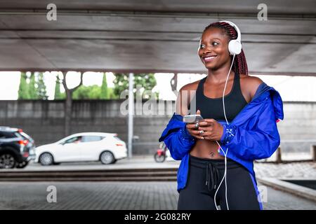 Lächelnde junge afroamerikanische athletische Frau, die auf dem Parkplatz Musik hört Stockfoto