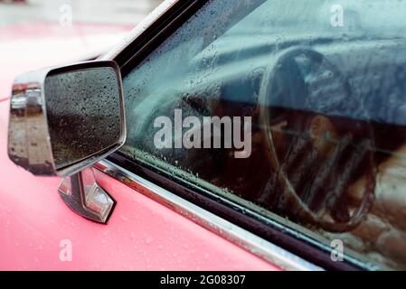 Detail eines Rückspiegels in klassischem Pink Auto an einem regnerischen Tag Stockfoto