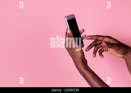 Crop Hände von afroamerikanischen Mann hält Telefon mit leer Bildschirm und Geste isoliert auf rosa Hintergrund Stockfoto
