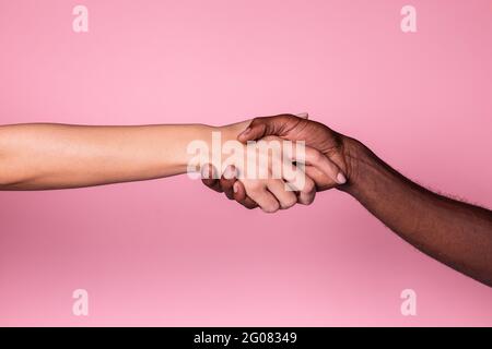 Multiethnische Hände von weißen Frauen und schwarzen Männern, die einen Handschlag auf rosa Hintergrund tun; Einheits- und Einbeziehungskonzept Stockfoto