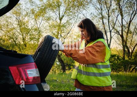 Das Mädchen wechselt das beschädigte Rad des Autos. Grünes Unterhemd. Reserverad. Verkehrsunfall. Anreise mit dem Auto. Stockfoto