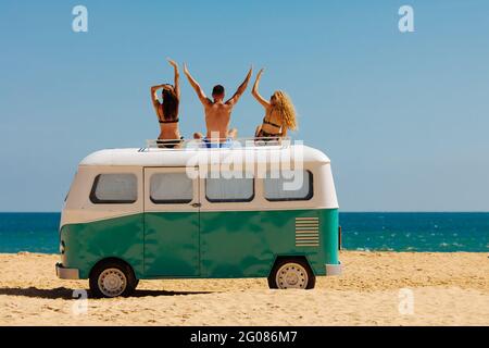Drei Touristen sitzen auf dem Dach eines Hippie-Autos am Sandstrand Stockfoto