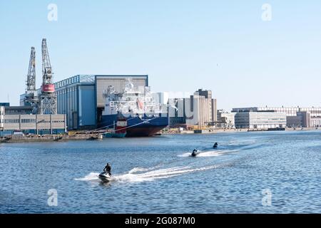 Menschen auf Wasserrollern im Westhafen von Helsinki, Finnland, gegen den Tanker Yuriy Kuchiev, der in der Arctech Helsinki Shipyard im Bau ist Stockfoto