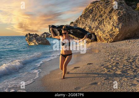 Junge, hübsche Frau, die während des Sonnenuntergangs an einem Sandstrand läuft Stockfoto