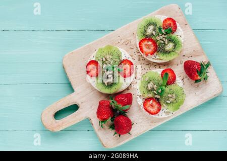 Sandwiches mit Kiwi, Erdbeeren und Sonnenblumenkernen auf Schneidebrett auf blauem Holztisch. Gesundes Frühstück. Draufsicht, flach liegend. Stockfoto