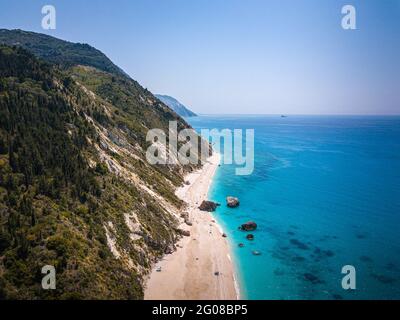 Drohnenaufnahme des wunderschönen kristallklaren türkisfarbenen und blauen Meerwassers, umliegender Felsen und Wellen, die den Sandstrand Megali Petra in Lefkada erreichen Stockfoto