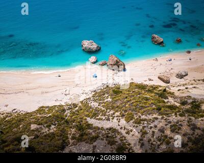 Drohnenaufnahme des wunderschönen kristallklaren türkisfarbenen und blauen Meerwassers, umliegender Felsen und Wellen, die den Sandstrand Megali Petra in Lefkada erreichen Stockfoto