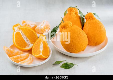 Orangefarbene Früchte mit orangefarbenen Scheiben und grünen Blättern auf weißem Hintergrund Stockfoto