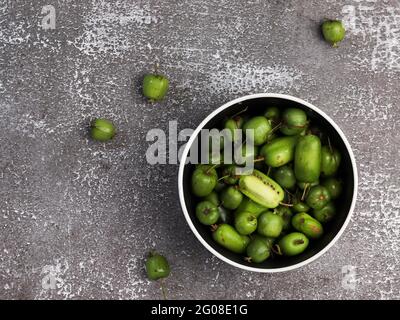 Mini-Kiwi-Babyfrucht (Actinidia arguta) in einer Schüssel auf dunklem Grund. Draufsicht, flach liegend Stockfoto