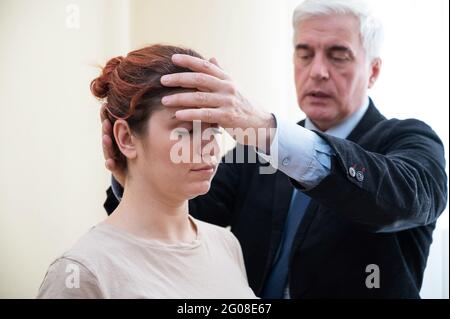 Reifer grauhaariger Mann hypnotisiert kaukasische Frau während der Hypnotherapie-Sitzung. Der Psychologe verwendet alternative Behandlungen für das Unterbewusstsein Stockfoto