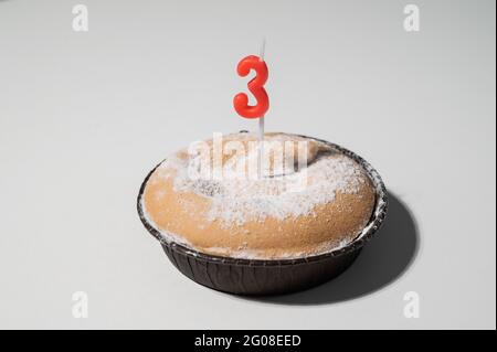 Kleiner Kuchen mit einer Kerze in Form der Nummer drei zum Geburtstag. Stockfoto