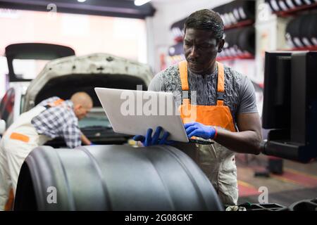 Afrikanischer Mechaniker, der in der Werkstatt ein Auto mit einem Laptop überprüft Stockfoto