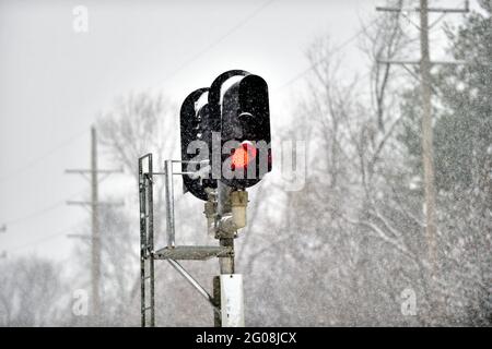 Genf, Illinois, USA. Ein rotes Eisenbahnsignal, das während eines Winterschneesturms auf der Hauptlinie der Union Pacific Railroad in einem Vorort von Chicago Halt signalisiert. Stockfoto