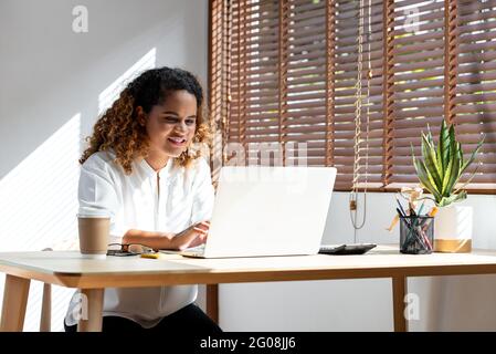 Glückliche junge afroamerikanische Geschäftsfrau, die von zu Hause aus auf einem Laptop im Wohnzimmer arbeitet Stockfoto