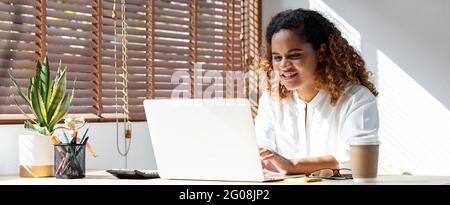 Bannerfoto einer glücklichen jungen afroamerikanischen Geschäftsfrau, die von zu Hause aus auf einem Laptop im Wohnzimmer arbeitet Stockfoto